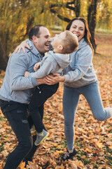 Fototapeta premium Happy family of three members resting in autumn city park posing against the beautiful yellow trees. Happy family outdoors. Activity relationship. Parent, child