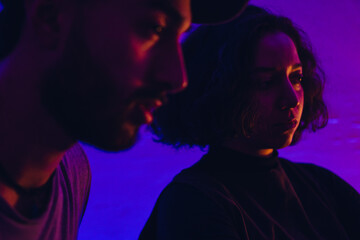 two young latinos a woman and a man in profile in a room with psychedelic colored lights