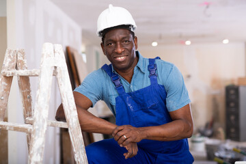 Portrait of confident african-american worker in blue overalls in a room being renovated