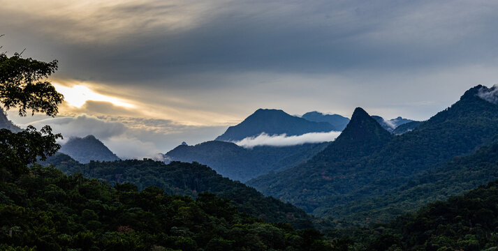 Fotografia horizontal do p&ocirc;r do sol numa floresta, onde se v&ecirc; as montanhas e as nuvens, uma paisagem absorvente e ic&oacute;nica de S&atilde;o Tom&eacute; e Principe