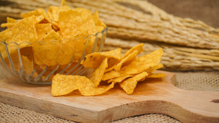Selicious nachos chips in glass bowl on a cutting board, isolated on burlap background