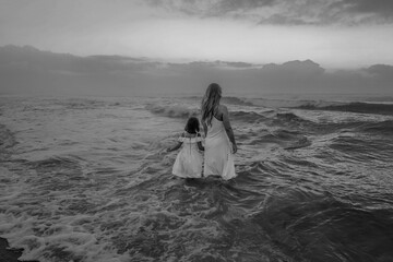 Brazilian Mother and daughter in white dresses walking together on the beach near the ocean. 