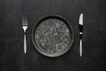 Silver knives and forks on a black background, empty iron plates.