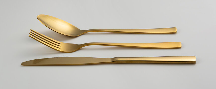 Gold knives, forks and spoons placed on a white background. Beautiful gold cutlery.