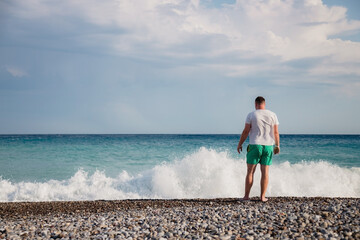 attractive young adult man stands with his back on the shore of the mediterranean sea with waves. copy space