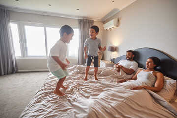 Mother, father and children jump on bed or bedroom and wake up happy together in family home in the morning. Happiness, love and smile of kids with parents in a house for real estate or holiday