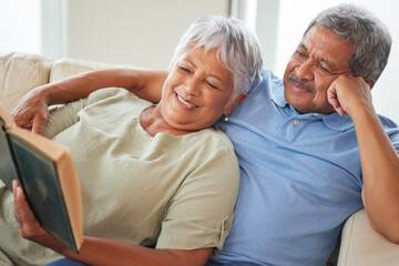 Relax, happy and senior couple reading a book together at home while relaxing and smiling on a...