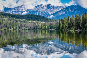 Reflections on Pyramid Lake in Jasper National Park with canoes nestled in the trees in the...
