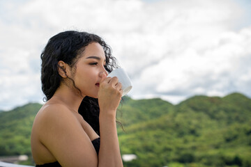 Young woman drinking a cup of coffee with a happy face standing and smiling with a confident smile. Woman drink coffee on roof top of condominium