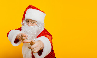 Santa claus points with index fingers at the camera on a yellow isolated background with copy space.