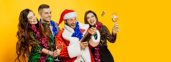 A group of young adult friends in New Year's tinsel and a santa costume shoot a champagne cork on a...