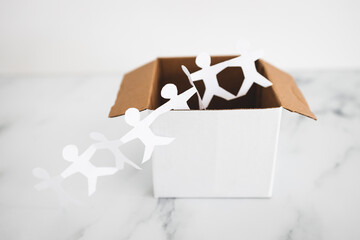 Think outside the box concept with paper people chain getting out of a white box on white marble