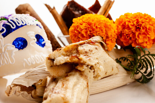 Close-up photo of a sweet split tamale in the background, a sugar skull and orange flowers, an image of a split tamale with a Day of the Dead decoration.