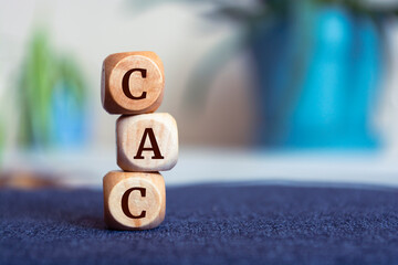 Tower made of cubes and dice with acronym CAC customer acquisition cost on wooden background