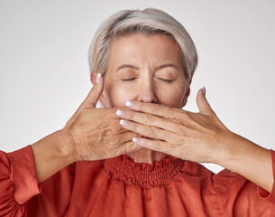 Senior, hands and mouth of an elderly woman covering her teeth or lips with hand against a grey studio background. Mature and aging woman keeping secrets, not talking and hiding the truth or gossip.