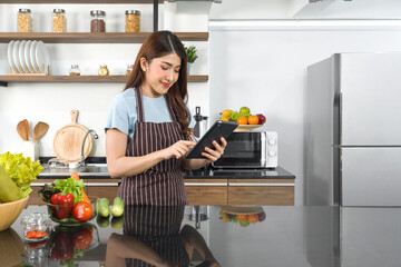 The housewife dressed in an apron  using tablet computer to find recipes on the internet. Morning atmosphere in a modern kitchen.