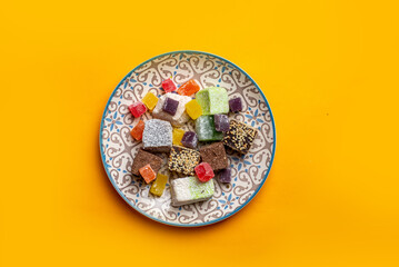 Turkish delight in cubes on a plate with oriental ornaments on a yellow background. Multicolored...