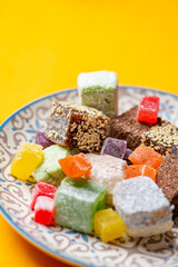 Turkish delight in cubes on a plate with oriental ornaments on a yellow background. Multicolored organic lokum oriental sweets. Close-up of sweets