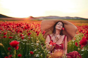 Portrait of a woman in a poppy field wearing a wide-brimmed hat at sunset. Front view.