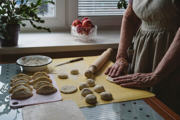 The hands of an elderly woman working with dough in the kitchen.