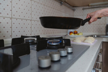 A close-up of a frying pan is placed on a gas stove with burning gas.