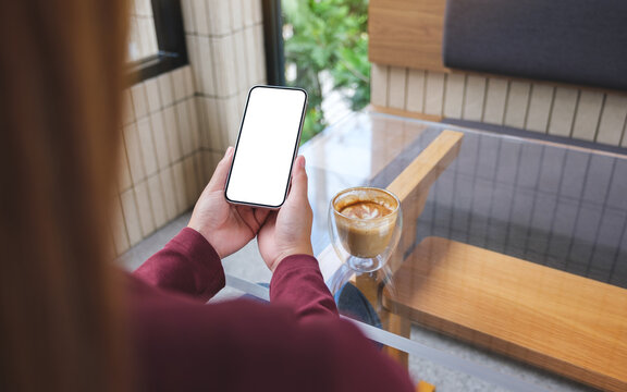 Mockup image of hands holding mobile phone with blank desktop screen with coffee cup on the table