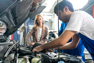 Fototapeta na wymiar Male car operator wearing blue overalls, gloves working under the hood of car and checking attentively serviceability of engine at repair garage. Concept of car maintenance