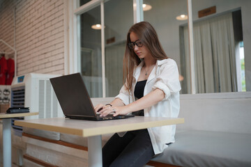 Technology and people concept, young woman using laptop and internet technology and sitting on the desk with laptop computer.