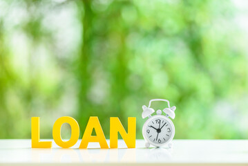Term loan for small business, financial concept : Alpabet letters, the word LOAN, a white alarm clock on a table, green bokeh background. Term loan provides borrowers with a lump sum of cash upfront. - obrazy, fototapety, plakaty