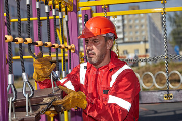 A specialist repairs the playground. A specialist in a white construction helmet and a red jumpsuit.