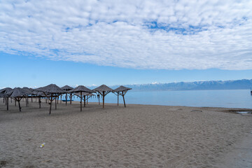 Deserted sandy beach with wooden umbrellas on the left at Issyk-Kul lake in Kyrgyzstan