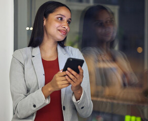 Thinking, phone and smiling woman texting, browsing the internet or using a mobile app with good network while working late at night. Hardworking entrepreneur checking investment growth online