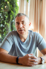 Aged businessman sitting at table in cafe with stylish watch and fitness wristband on hands. Handsome gray haired 50 years old man resting in cafe. Modern lifestyle, business people, public catering