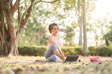 Naklejka na ściany i meble Beautiful young Asian woman healthy in sportswear doing use tablet for yoga or workout practice in park outdoor under sunset. Healthy lifestyle and relaxation.