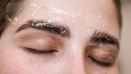 Caucasian woman on the procedure of permanent styling and coloring of eyebrows.