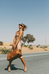 A stylish young woman in sunglasses and with a bag in her hands on a deserted road