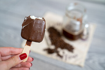 blur background, woman hand with manicure holds half eaten ice cream and pours it into strong black coffee espresso shot in glass cup, set on table, long spoon and coffee beans on napkin, affogato