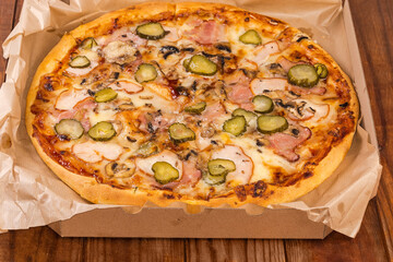 Pizza with different ham in cardboard box on rustic table