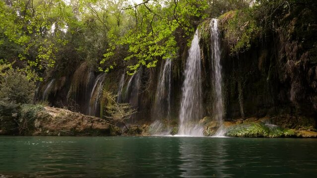 Time lapse shot of Kursunlu Waterfall, many rather small water flows at spring season, dim light in shadow of the trees. Green colour of pond water