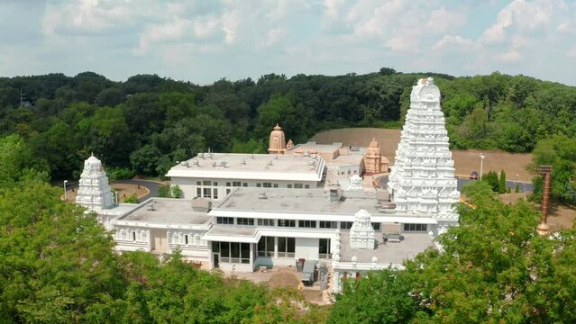 Aerial drone shot of the side of a south Indian hindu temple surrounded by green forest at daytime.
