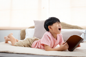  An Asian boy, handsome, laying in his favorite soft bed reading a book, He put the book down on the bed, and rubbing both eyes with both hands, boredom with reading made him sleepy.