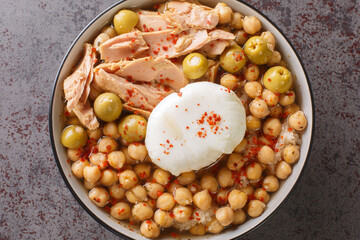 Chickpeas in broth served with canned tuna, olives and poached egg close-up in a bowl on the table. Horizontal top view from above