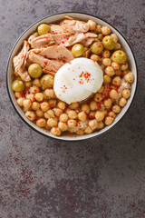 Tunisian dish Lablabi or Lablebi based on chick peas in a thin garlic and cumin broth topped with a poached egg and tuna closeup in the bowl on the table. Vertical top view from above