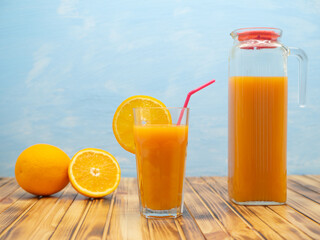 Glass of orange juice, jug and ripe oranges on wooden table