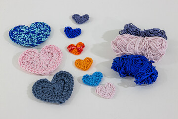Set of handmade crochet hearts of different colors and sizes next to blue, pink and gray cotton...