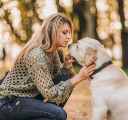 A young blonde woman is playing in the autumn park with her labrador. Evening walk with a labrador.