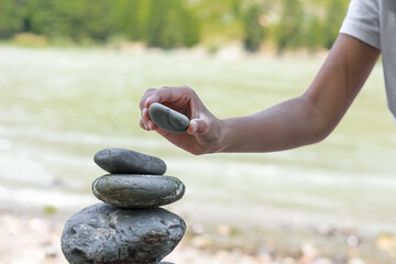 Girl hand picking up set zen stones, relaxed hobby restoring. Building stacked stones on the river bank. Meditation and harmony.