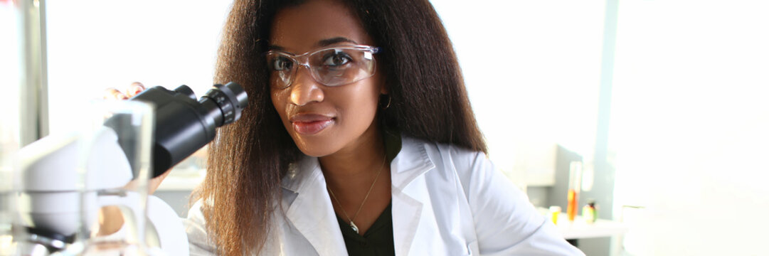 Black Woman Scientist In Goggles, Conducts Study Using Microscope
