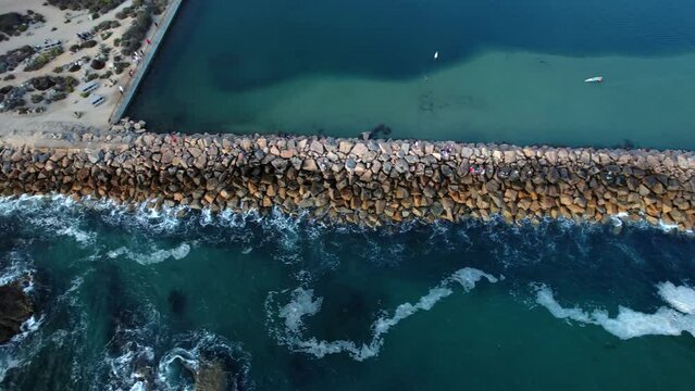 A rocky ocean jetty stretching out into the Pacific Ocean - aerial tilt down sliding reveal