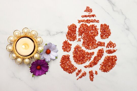 Ganesha art is made with colored rice. Ganesh Chaturthi wallpaper or banner. Ganpati over yellow and white background along with diya and flowers. copy space.